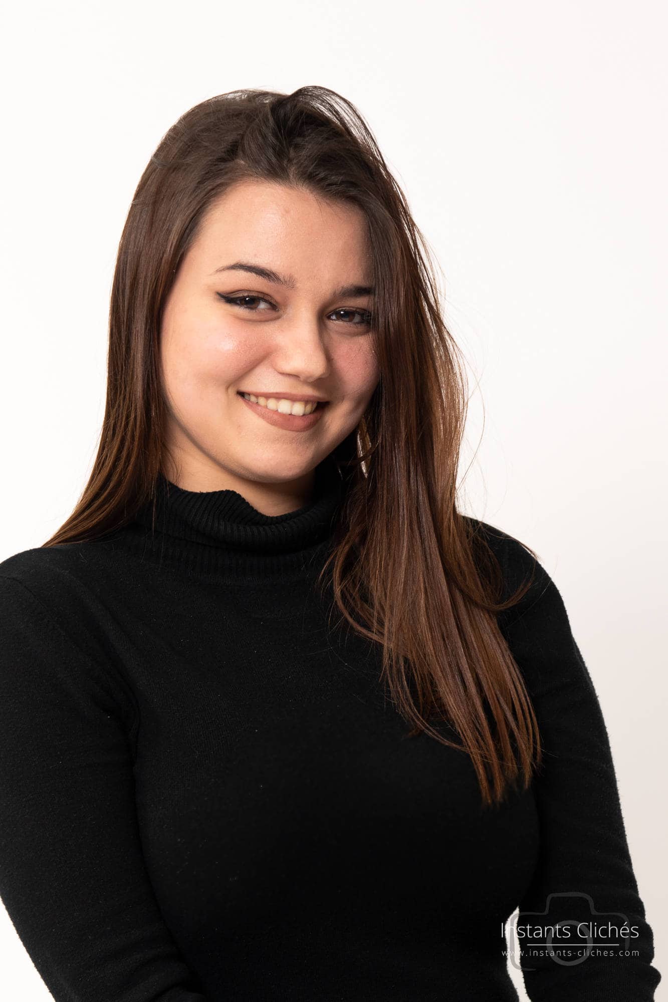 Portrait d'une femme souriante en noir contre fond blanc.